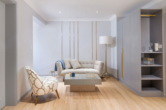 Sala de estar, com uma poltrona com um padrão simples em dourado e branco, um sofá cinzento claro, um móvel cinzento claro e chão em madeira, no apartamento renovado em Telheiras.