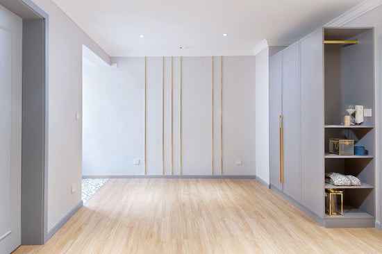 Sala de estar renovada, com o chão em madeira e as paredes cinzentas claras com detalhes em dourado, no apartamento renovado em Telheiras.